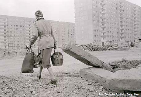 Karl-Marx-Stadt. Eine Frau läuft mit schweren Taschen über ein ungepflegtes Gelände in einem Neubauviertel, 1978
