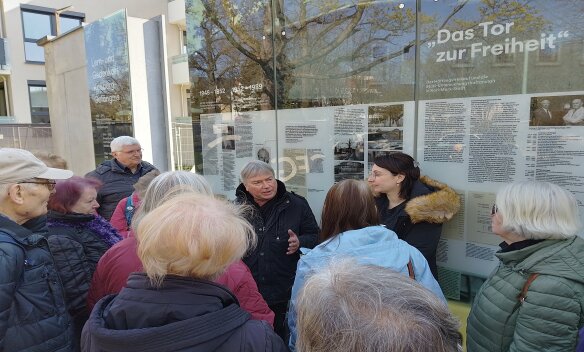 A group of visitors talking to a contemporary witness at the memorial site, which is located on the outer wall of the former Kaßberg prison on Chemnitz's Kaßberg.