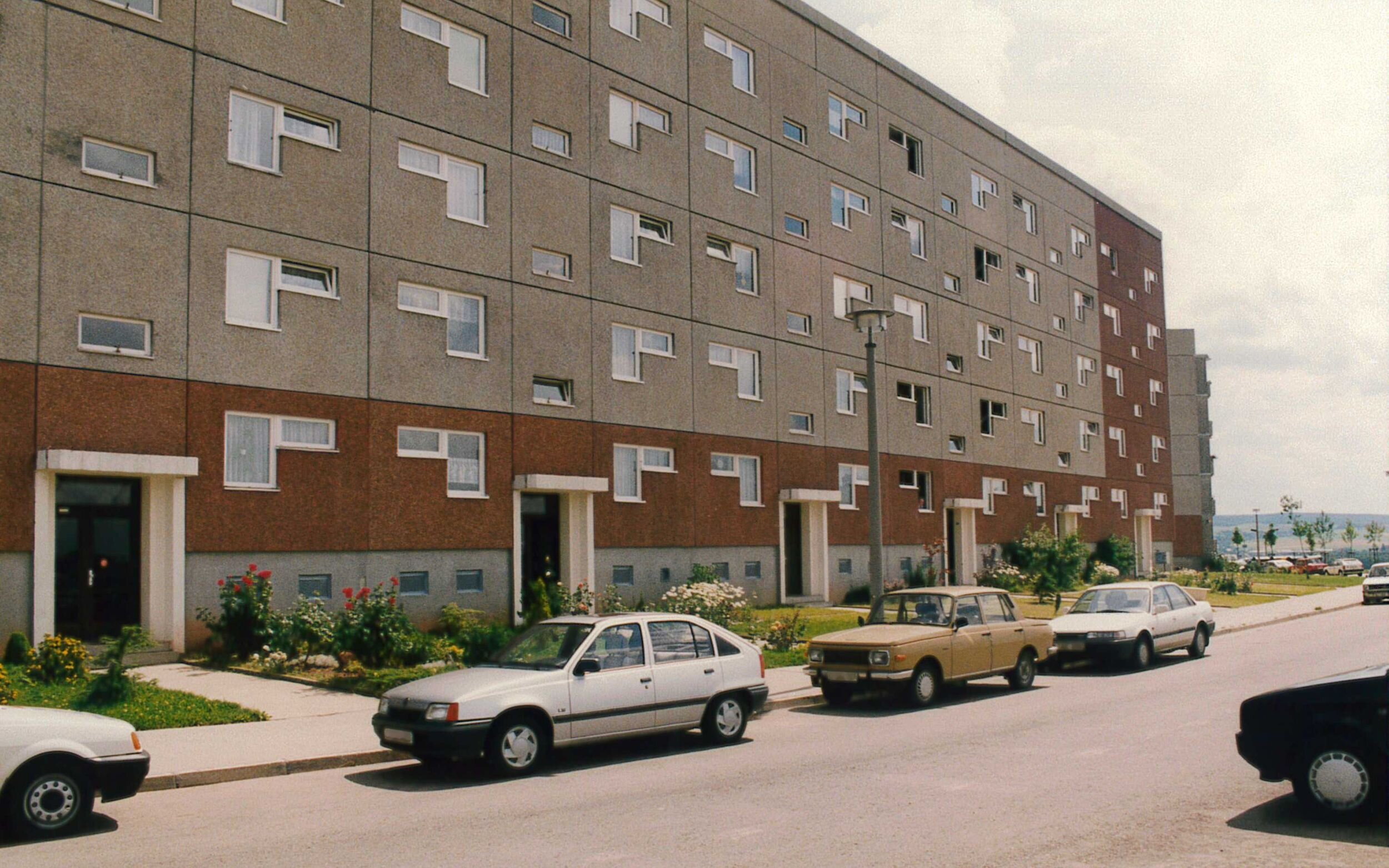 Vor den Eingangstüren eines Wohnblocks auf der Max-Opitz-Straße 11-29 stehen am Straßenrand parkende Fahrzeuge. Die Aufnahme entstand Anfang der 1990er Jahre.
