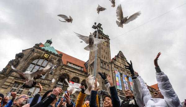 Vor dem Rathaus entlassen Chemnitzerinnen und Chemnitzer Friedenstauben in die Lüfte. Der Himmel ist bewölkt.